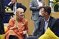 Ein Mann und eine Frau sitzen auf grauen Sesseln mit gelben Kissen und unterhalten sich.