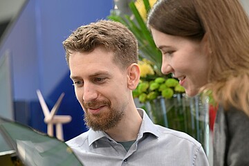 Zwei Personen betrachten gemeinsam eine digitale Präsentation an einem Messestand.