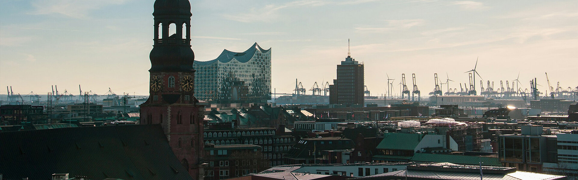 Keyvisual des RECHARGE Wind Power Summit. Blick auf die Hauptkirche St. Michaelis, die Elbphilharmonie und den Hamburger Hafen. Im Hintergrund sind Windräder zu sehen.