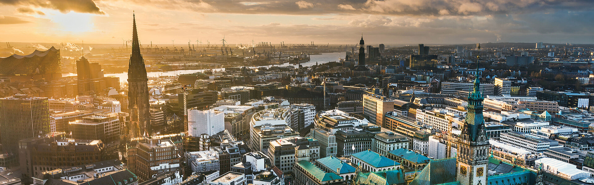 Keyvisual des RECHARGE WindPower Summit. Blick auf Hamburg mit der Hauptkirche St. Michaelis, der Elbphilharmonie, dem Hamburger Hafen und dem Rathaus. Im Hintergrund sind Windräder zu sehen.