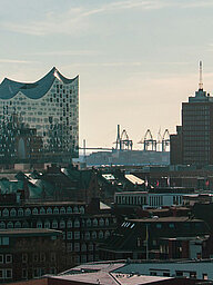 Keyvisual des RECHARGE Wind Power Summit. Blick auf die Hauptkirche St. Michaelis, die Elbphilharmonie und den Hamburger Hafen. Im Hintergrund sind Windräder zu sehen.