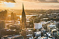 Keyvisual des RECHARGE WindPower Summit. Blick auf Hamburg mit der Hauptkirche St. Michaelis, der Elbphilharmonie, dem Hamburger Hafen und dem Rathaus. Im Hintergrund sind Windräder zu sehen.