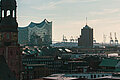 Keyvisual des RECHARGE Wind Power Summit. Blick auf die Hauptkirche St. Michaelis, die Elbphilharmonie und den Hamburger Hafen. Im Hintergrund sind Windräder zu sehen.